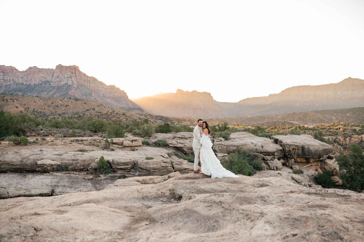 Zion Adventure Session. Panoramic desert landscape with wedding couple posing on rocky outcrops at sunset.