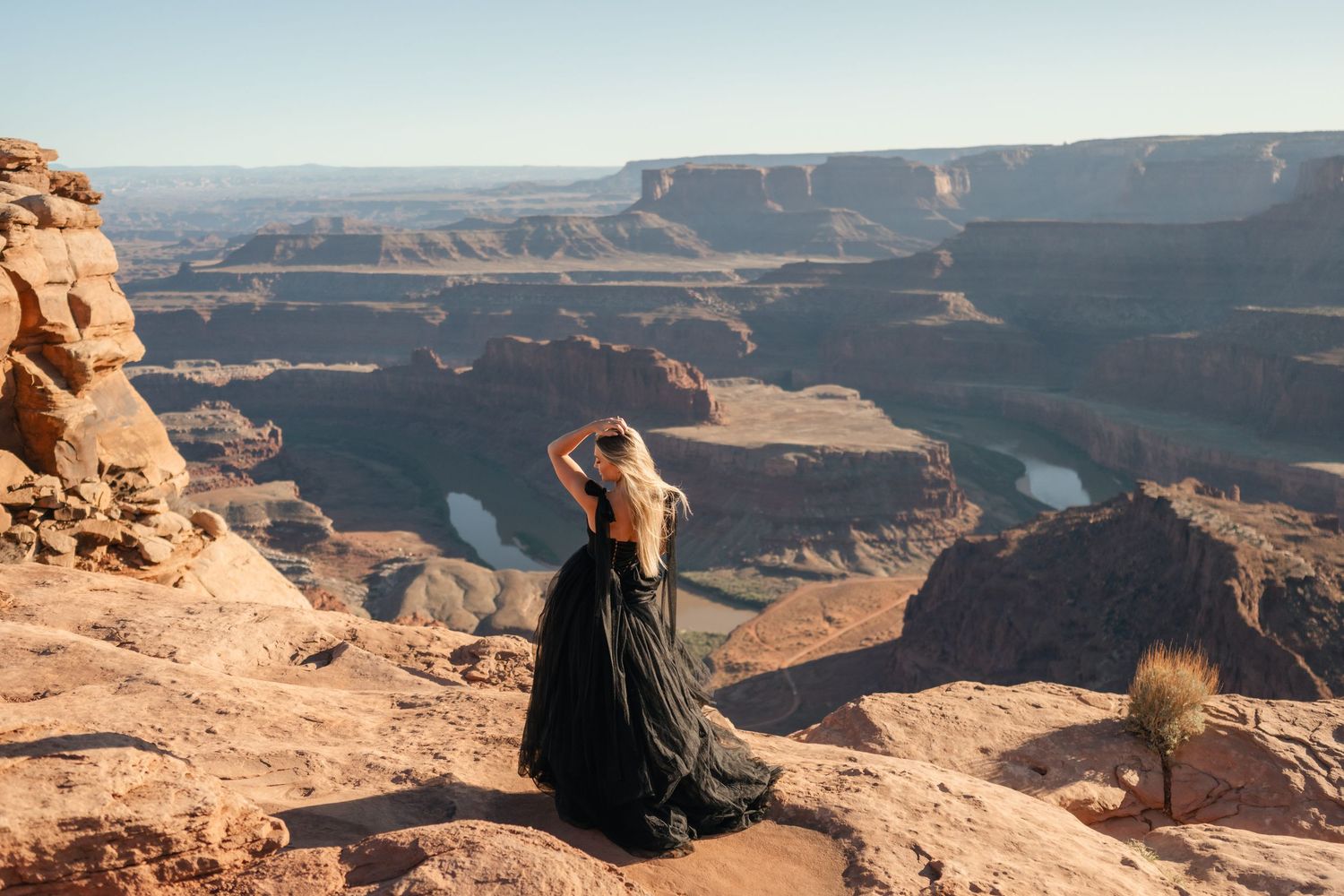Person sits on edge of Grand Canyon cliff overlooking vast desert landscape and deep canyon walls at sunset.