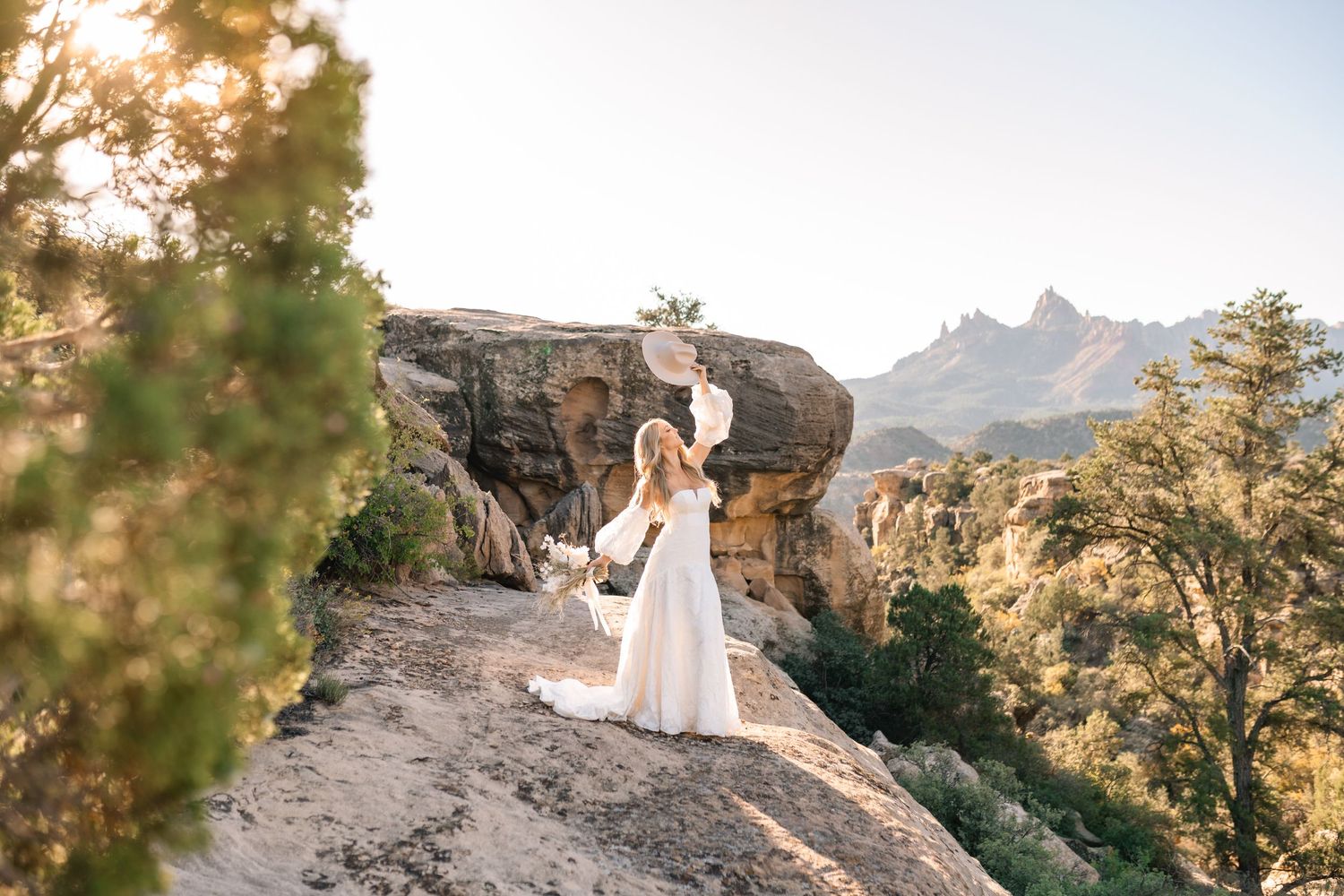 Ethereal bridal photo on rocky cliff overlook with mountain peaks in background.