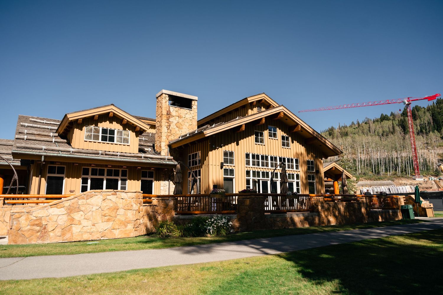 Rustic mountain lodge with wooden beams and stone accents sits against backdrop of mountains on a sunny day. Park City Wedding Photographer.