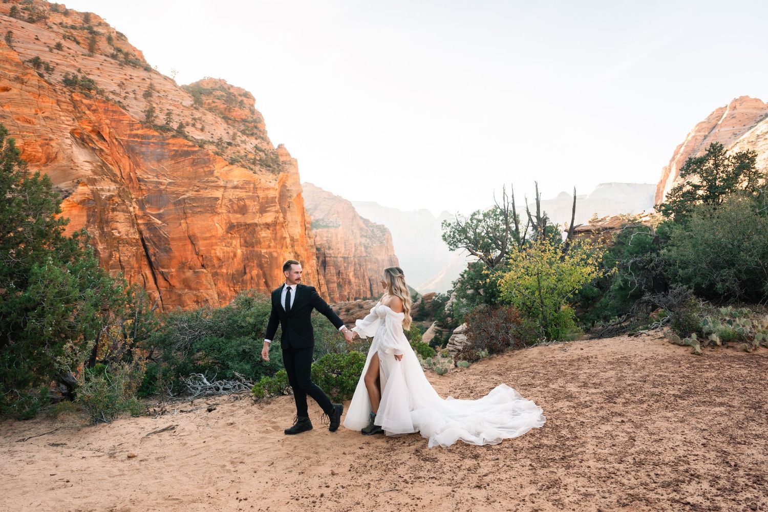Couple walking hand in hand through desert landscape during sunset wedding shoot.