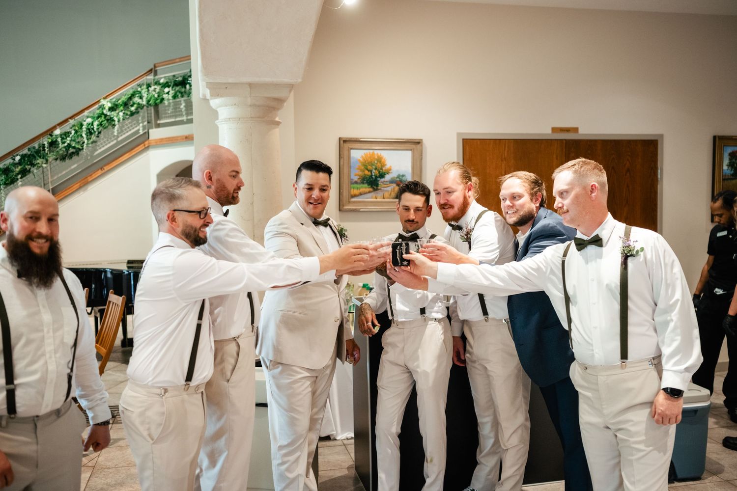 A group in white suits and suspenders sharing a celebratory toast in an elegant indoor setting.