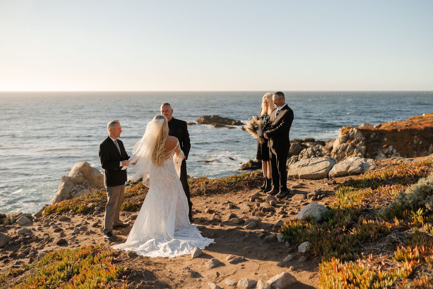 Wide angle shot of a coastal wedding ceremony with ocean waves and golden light.
