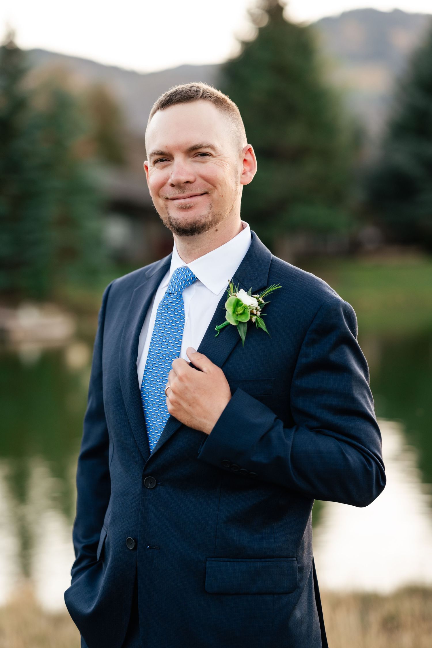 Formal event photography session near a serene lake with mountains and evergreen trees in the background.