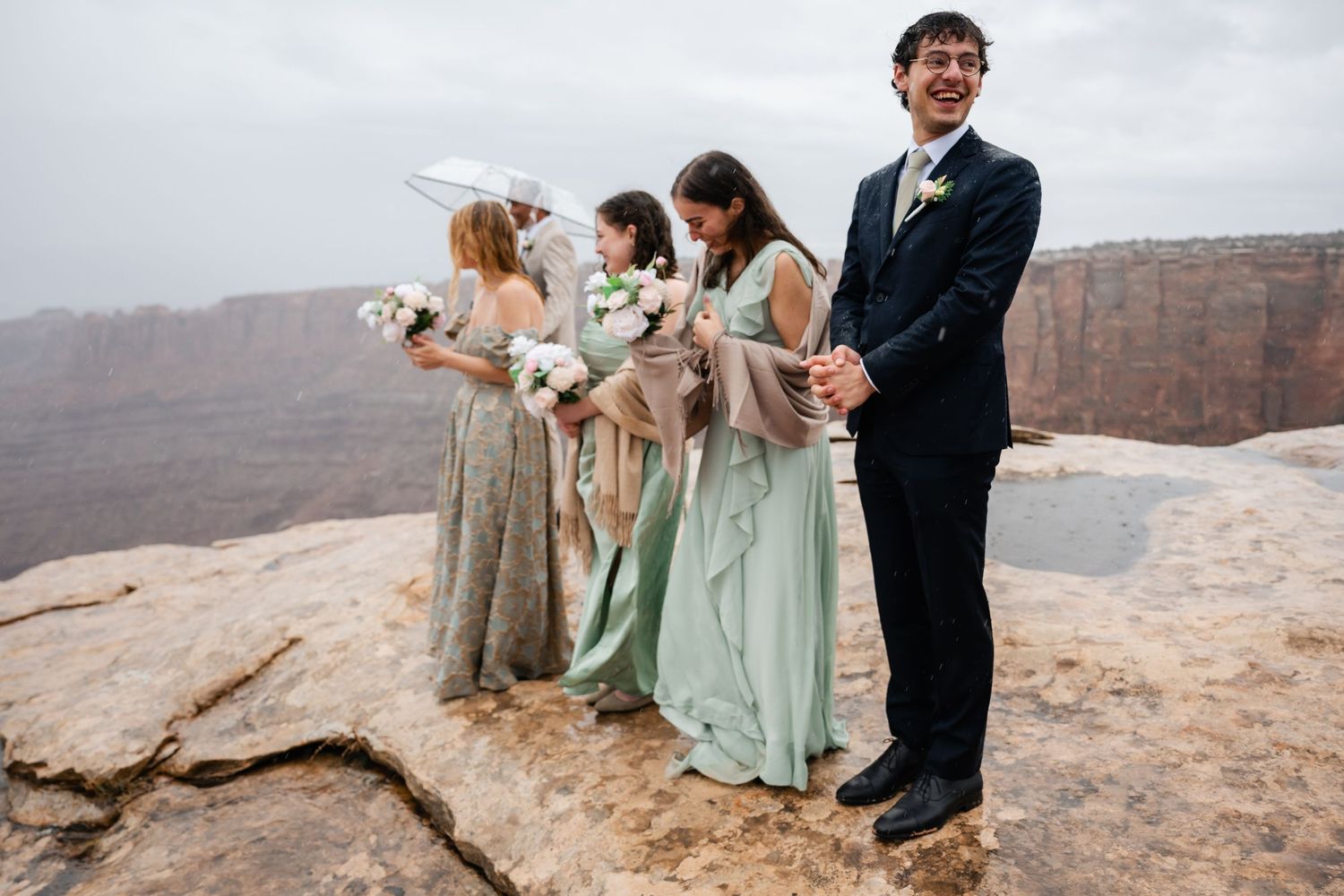 Wedding party stands on cliff edge with dramatic canyon views in the background.