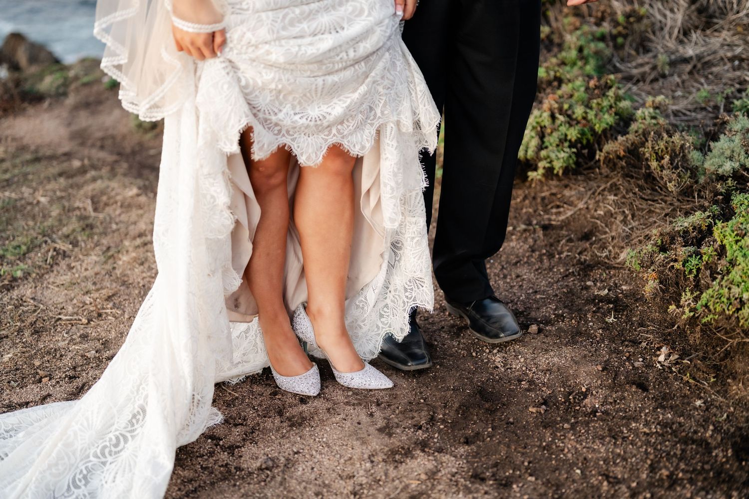 Detail shot of wedding attire and footwear against coastal backdrop.
