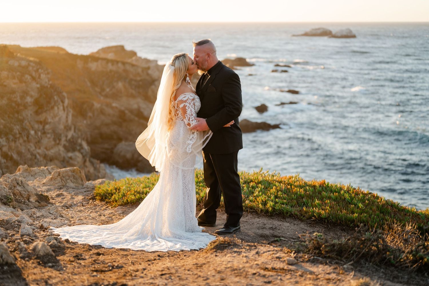 Wedding couple sharing an intimate moment on rocky coastal cliffs during golden hour.