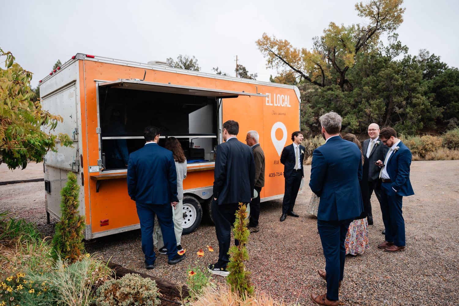 A bright orange food truck parked outdoors with people gathered around it during an event.