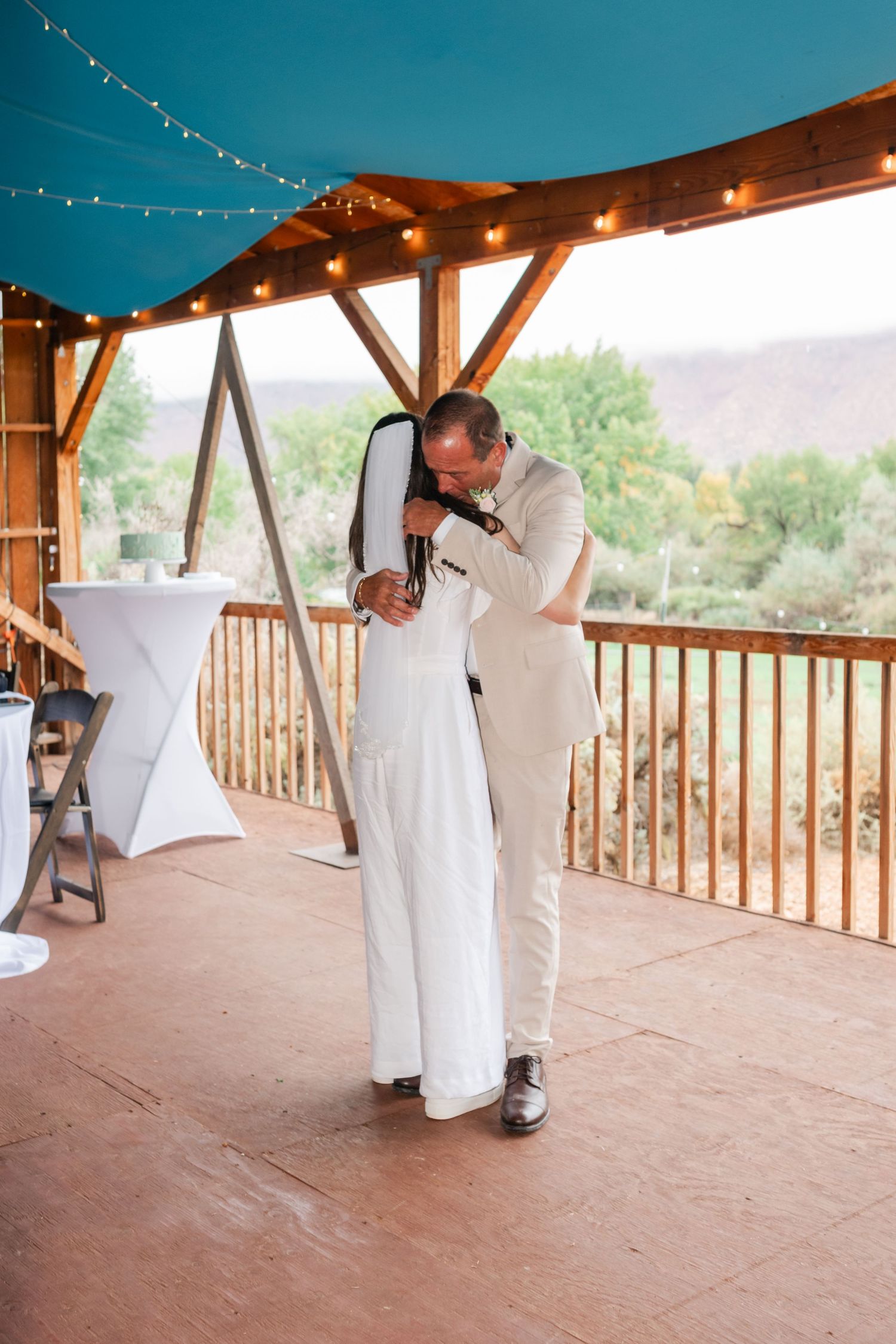 Couple shares an intimate dance moment on a rustic wooden deck with string lights and mountain views.