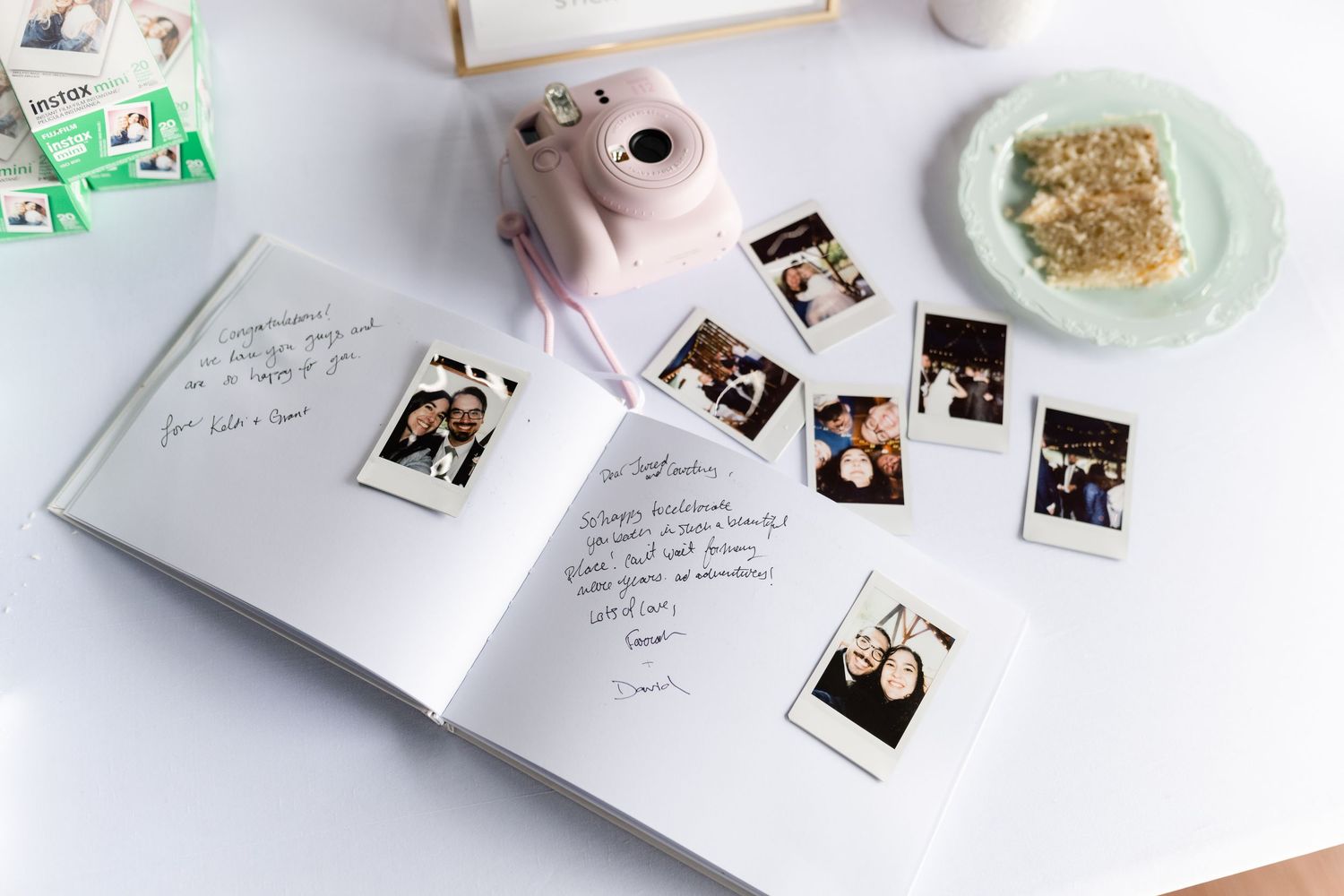 Wedding reception table with polaroid photos, guestbook, and pastel decorative elements.