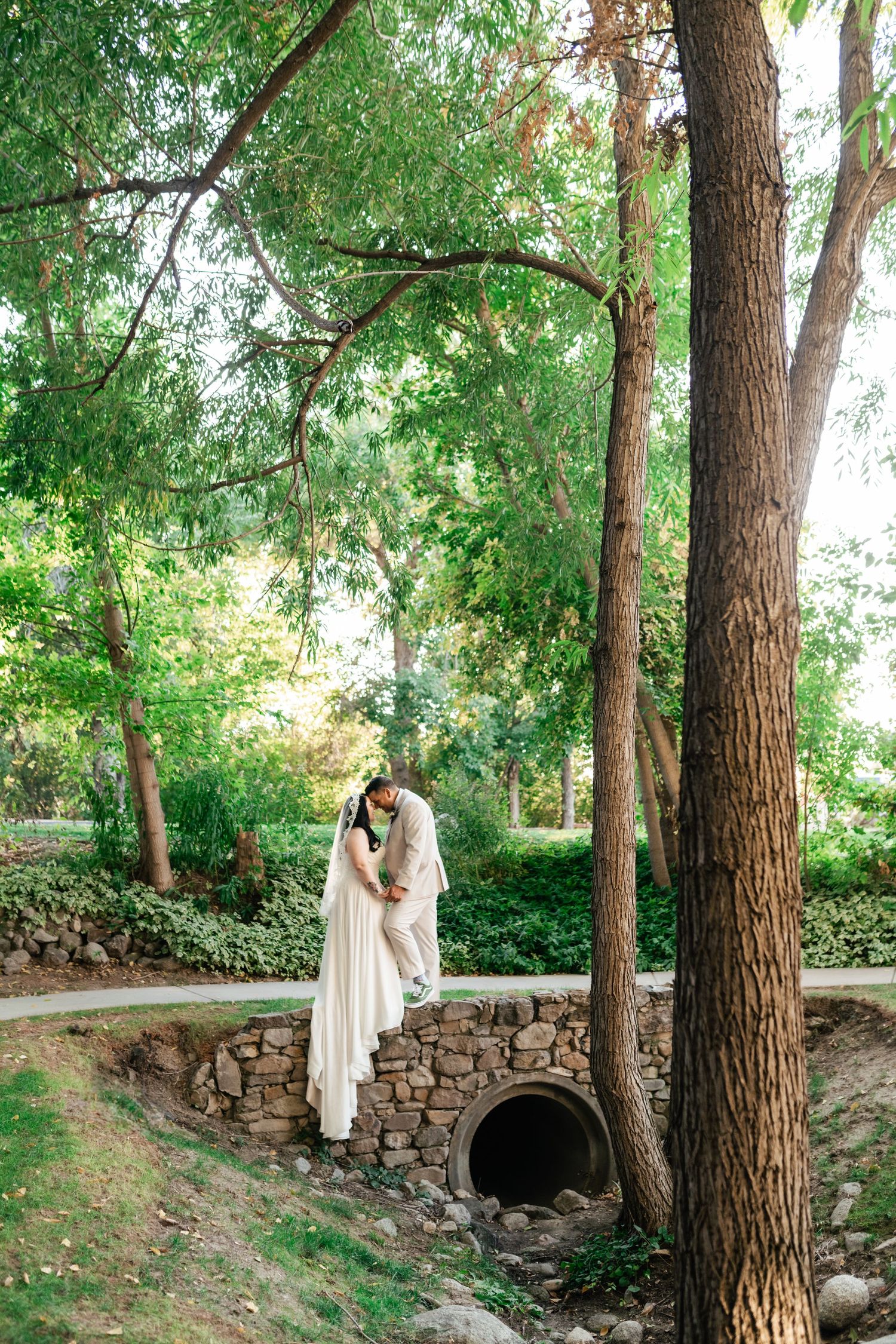 A romantic outdoor photoshoot in a wooded area with stone walls and tall trees creating a natural, serene backdrop at Alpine Art Center.