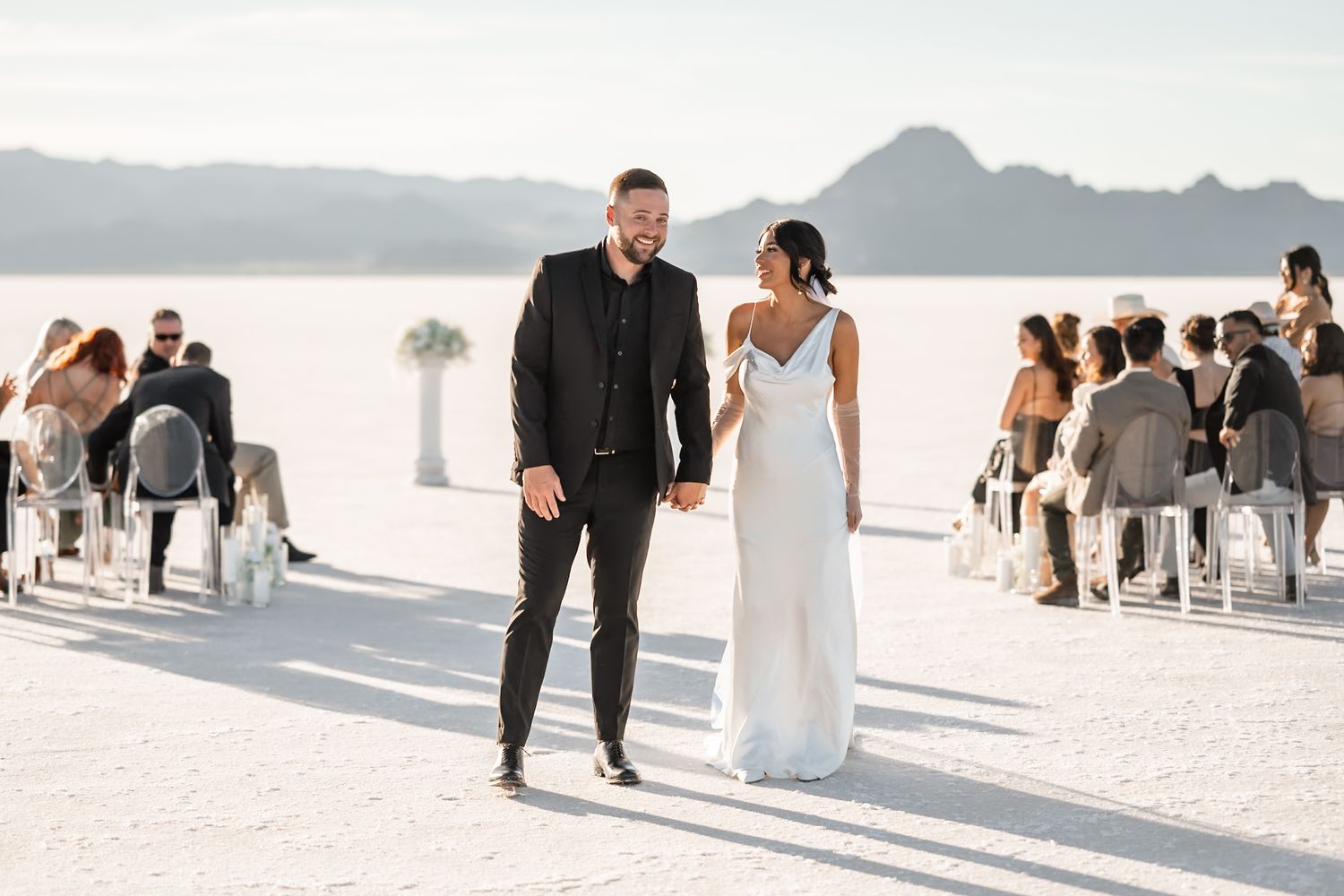 Couple walking down aisle on salt flats after desert wedding ceremony.