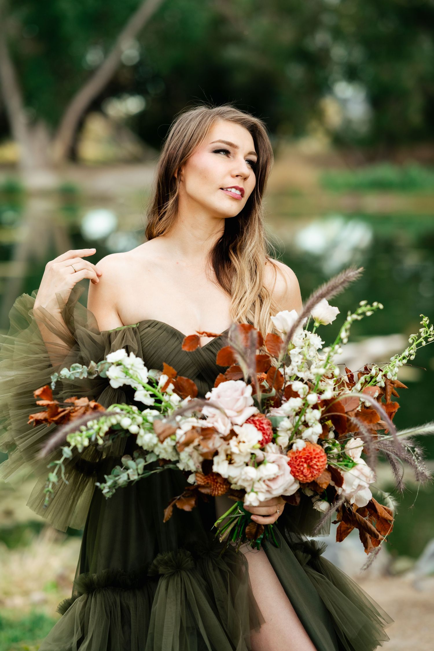 A bride in an olive green dress holds a stunning autumn bouquet with white and orange flowers. Unique wedding photographer.
