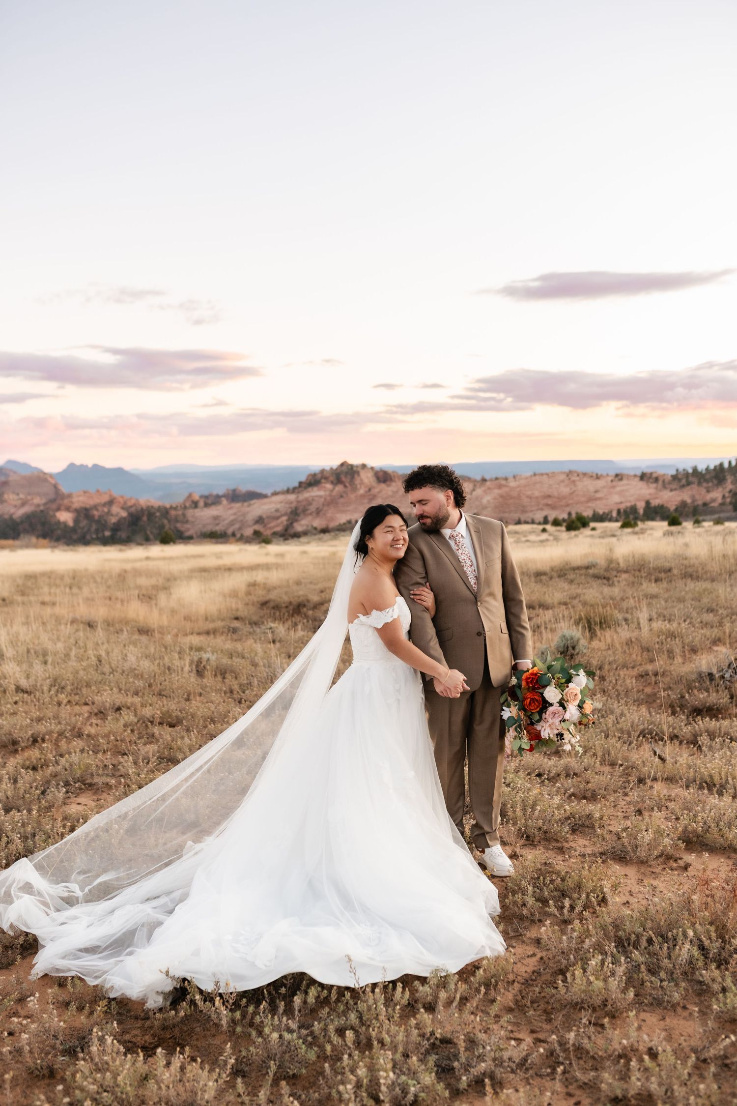 Romantic wedding photography in a rustic field with mountains and sunset sky in the background.