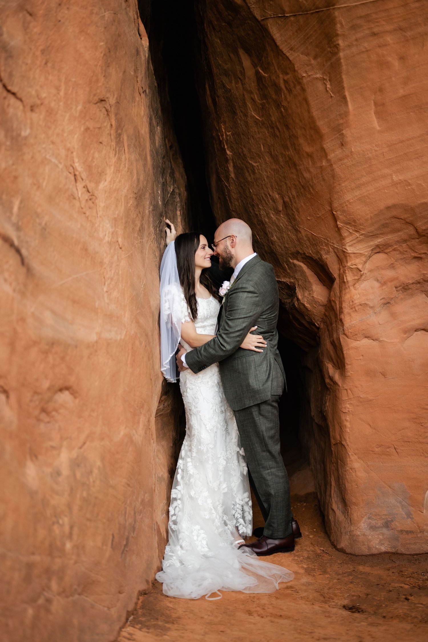 A romantic wedding couple shares intimate moments in a red rock cave formation at their desert elopement. Utah elopement photographer.