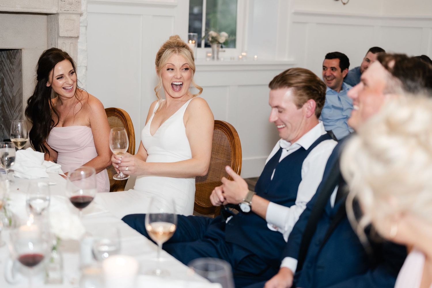 Joyful moment captured during wedding reception speeches in elegant white dining room.