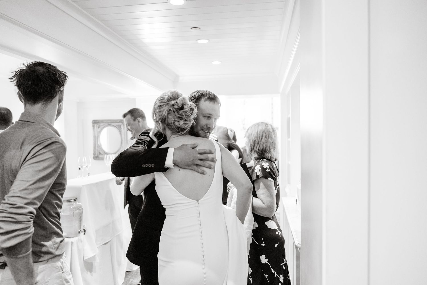 Wedding guests stand and embrace during an emotional moment at an indoor ceremony.