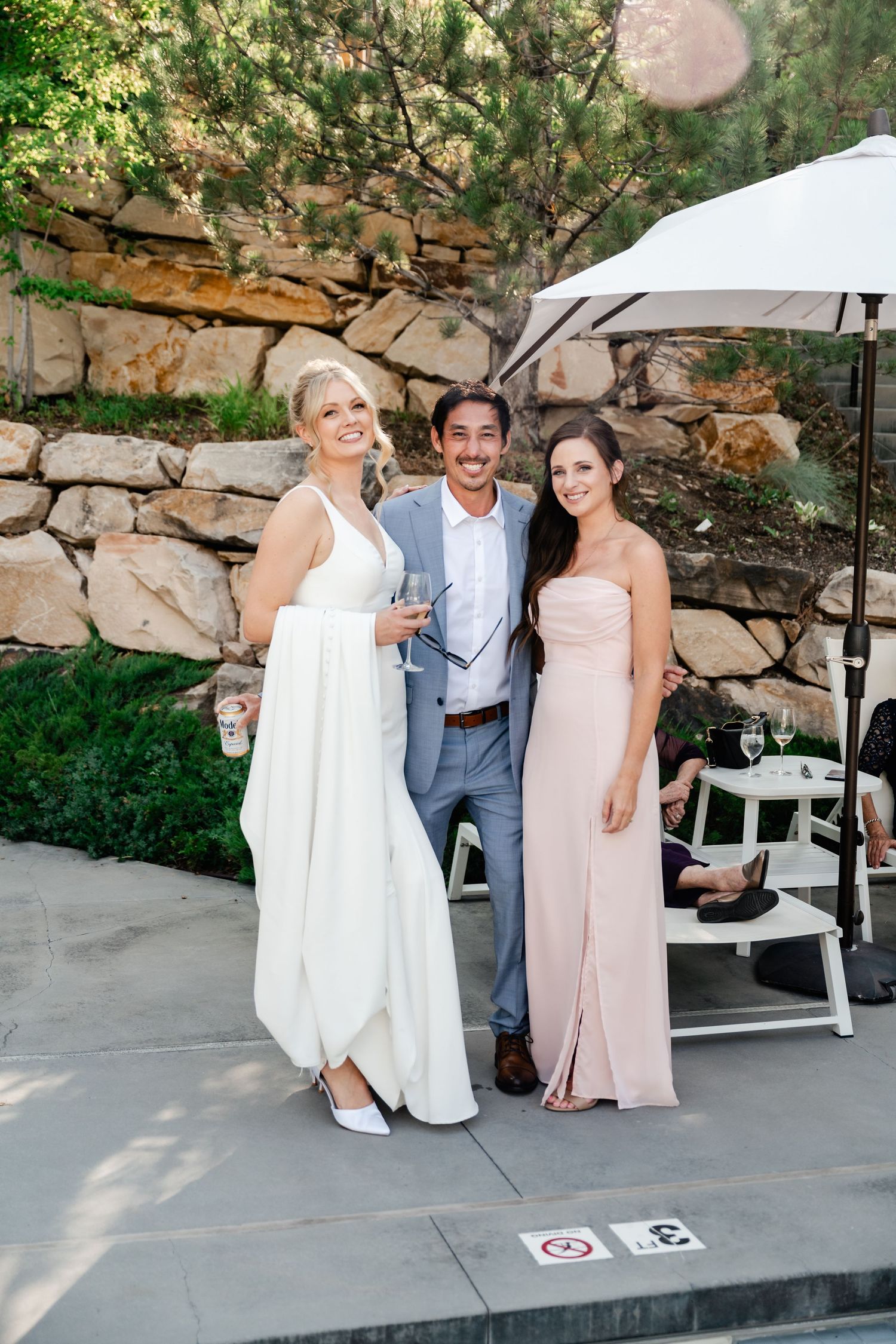 Wedding party poses outdoors against a stone wall backdrop during sunset.