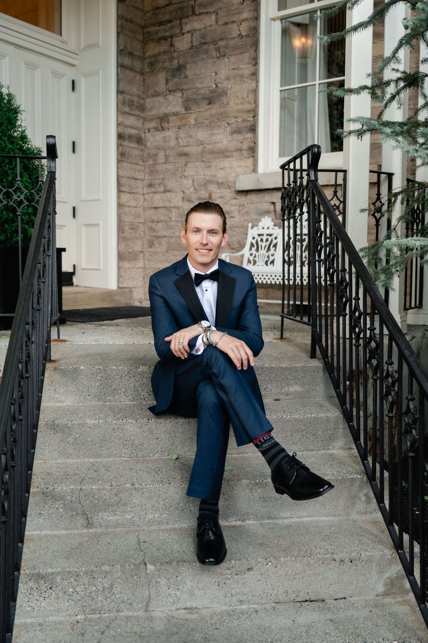 Groom in navy suit sitting on stone steps with playful expressions.