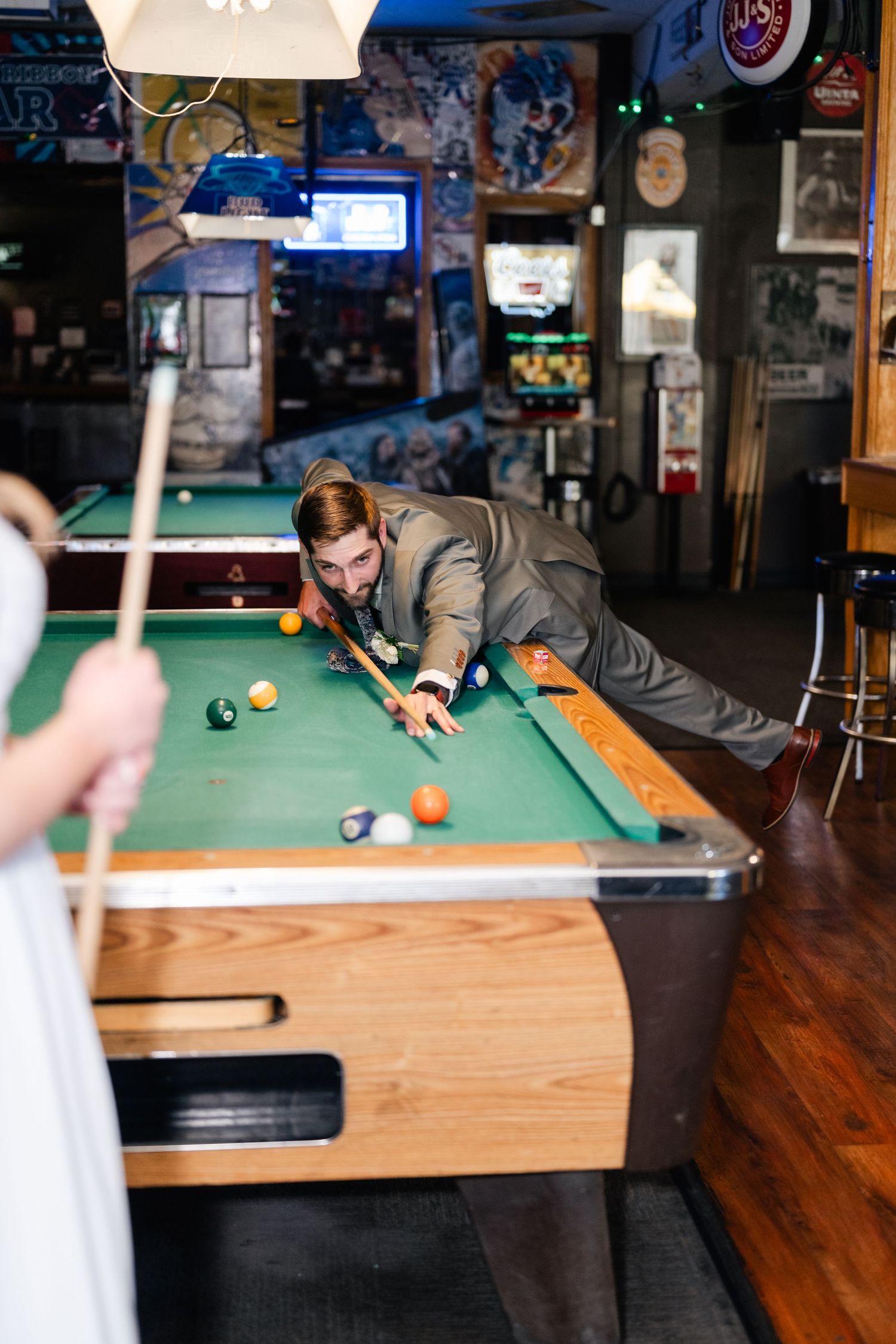 Someone in a gray suit takes a challenging pool shot on a green felt table.