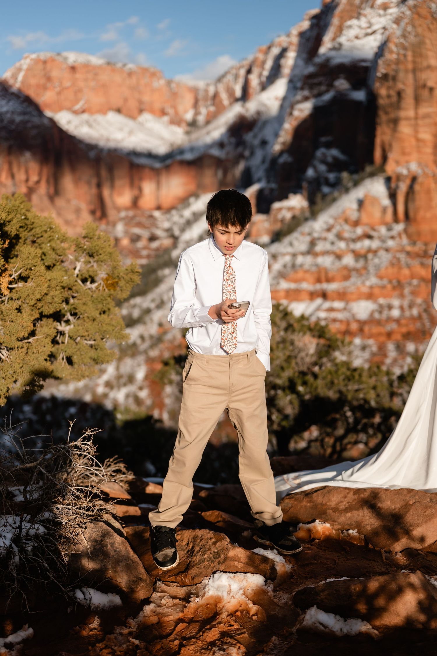 Person in white and tan attire poses against dramatic red rock cliffs and snow.