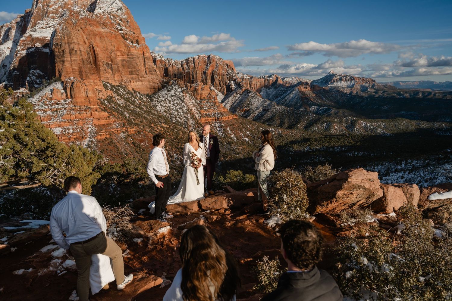 Panoramic view of red rock cliffs and snow-capped mountains under a bright blue sky.