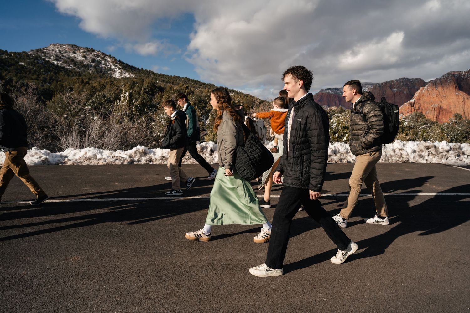 People playing and walking along a snowy path with red rock formations in background.