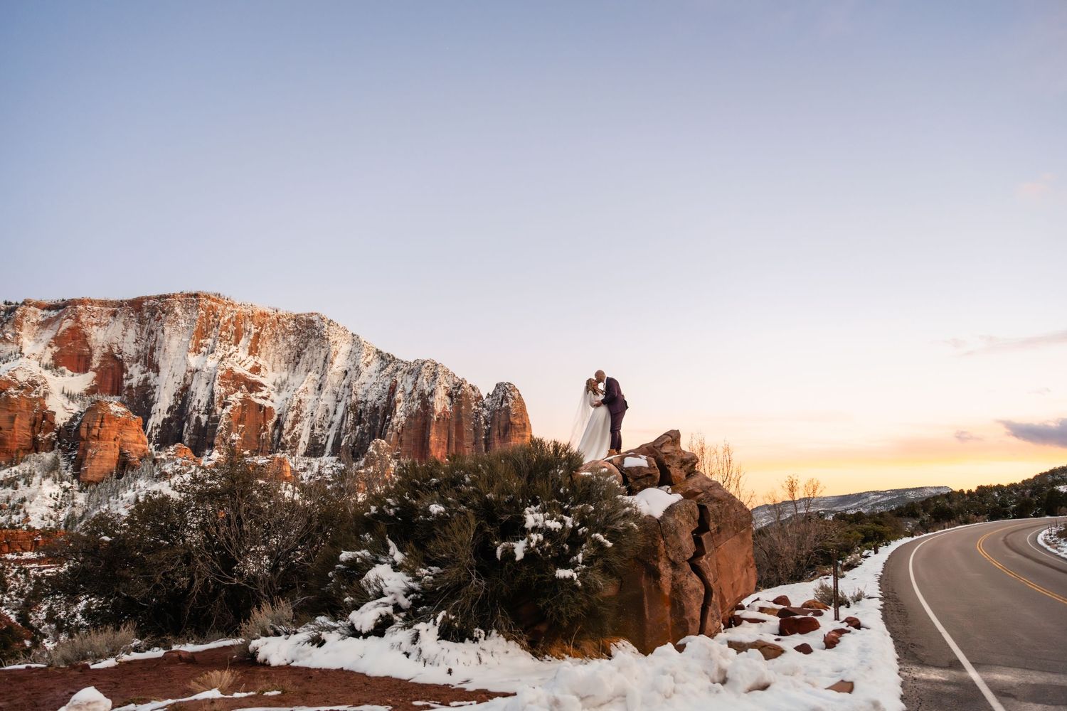 Scenic winter landscape of snow-covered red rock formations along a winding mountain road.