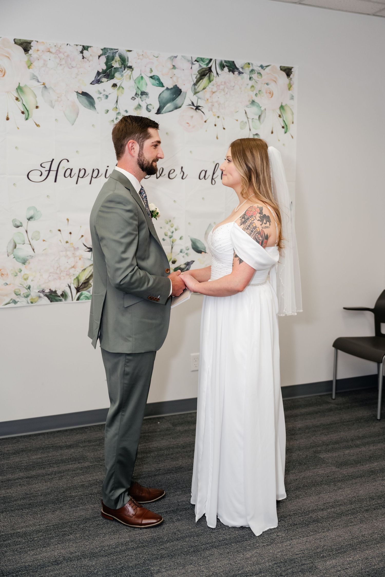 A couple shares a first look moment in a room with floral wall decor and gray carpeting.