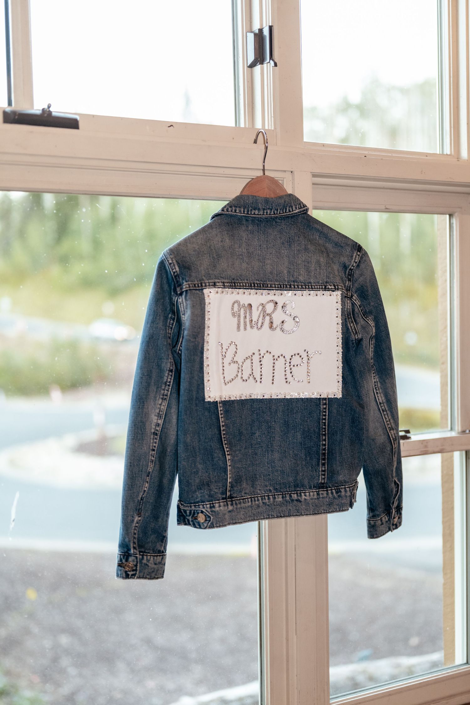 Personalized denim jackets hanging in window display for wedding celebration.