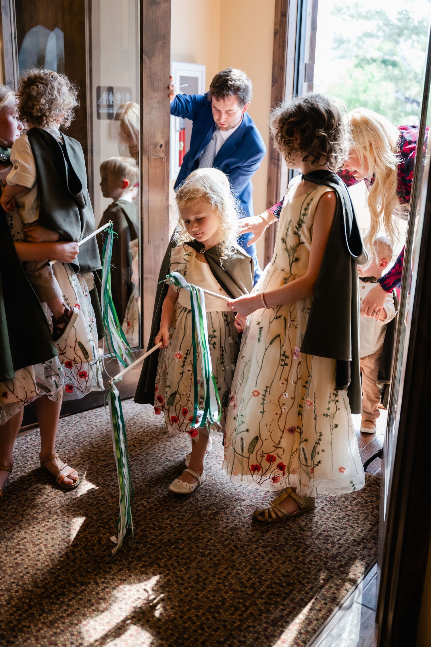 Wedding guests in floral dresses holding green ribbons in a church hallway.