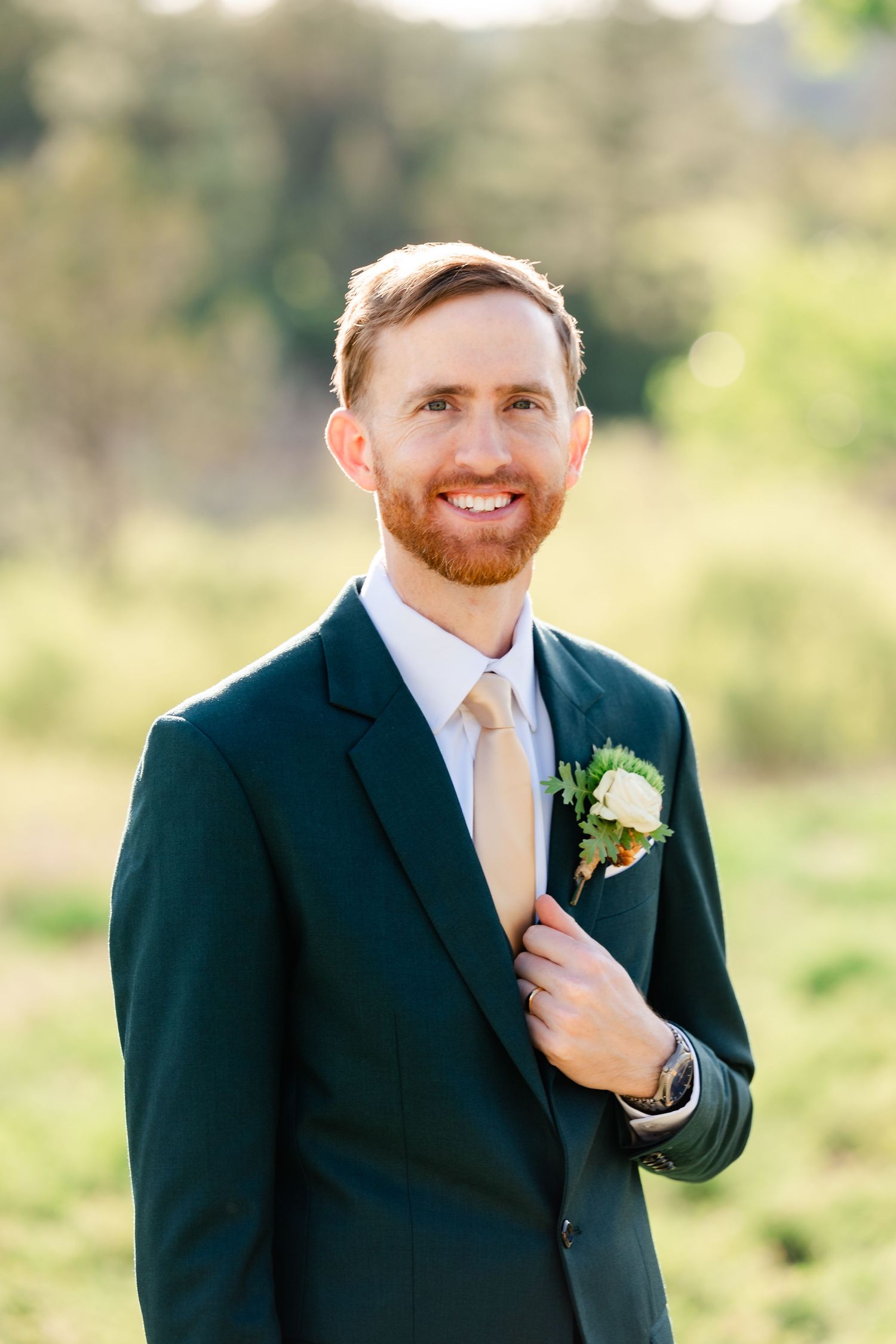 A groom in a dark suit and yellow tie smiles warmly at the camera.