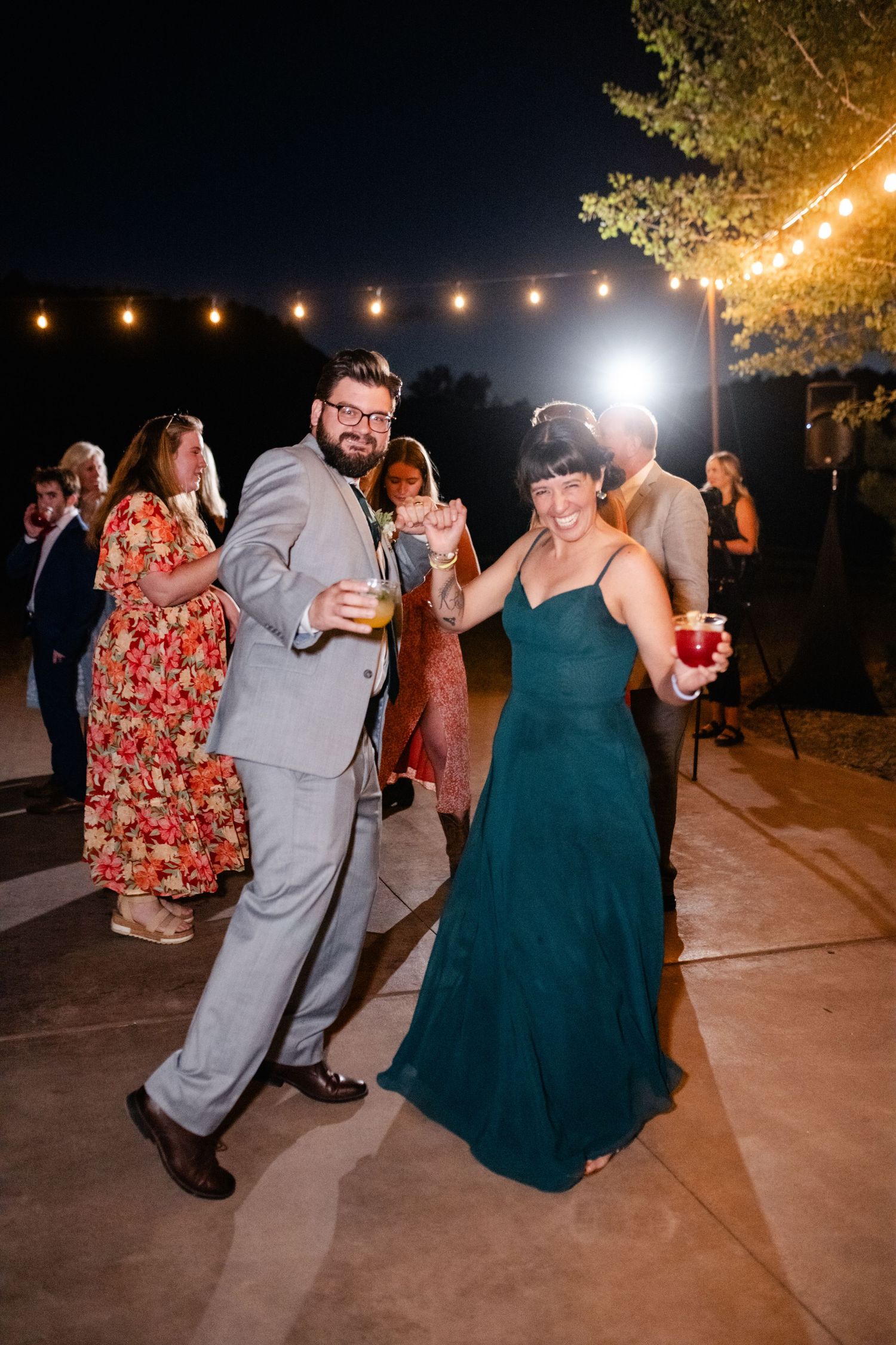 Wedding guests dancing and celebrating on an outdoor patio under string lights at night.
