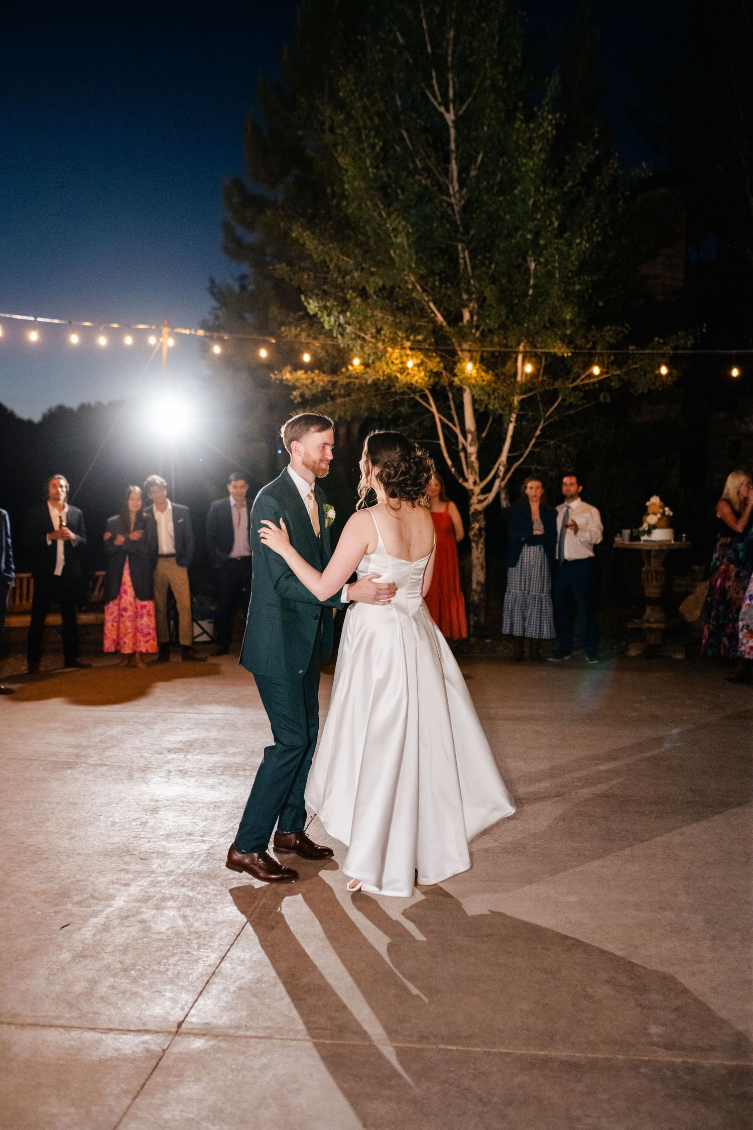 Couple sharing their first dance on an outdoor patio under string lights at night.