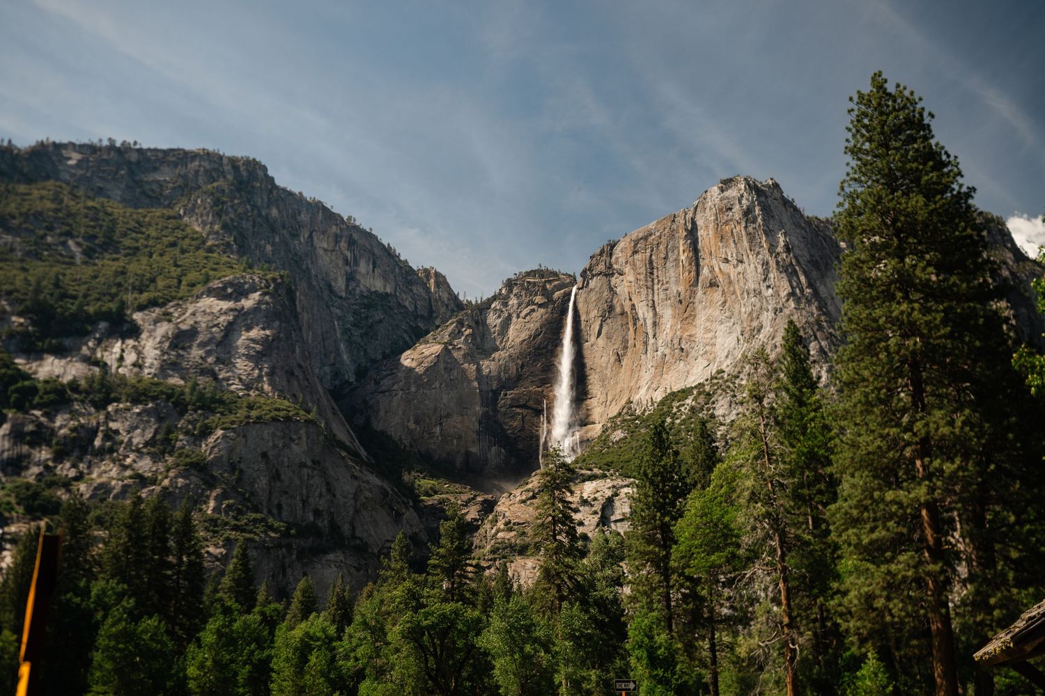 Majestic Yosemite Falls cascading down granite cliffs surrounded by tall pine trees under a blue sky.