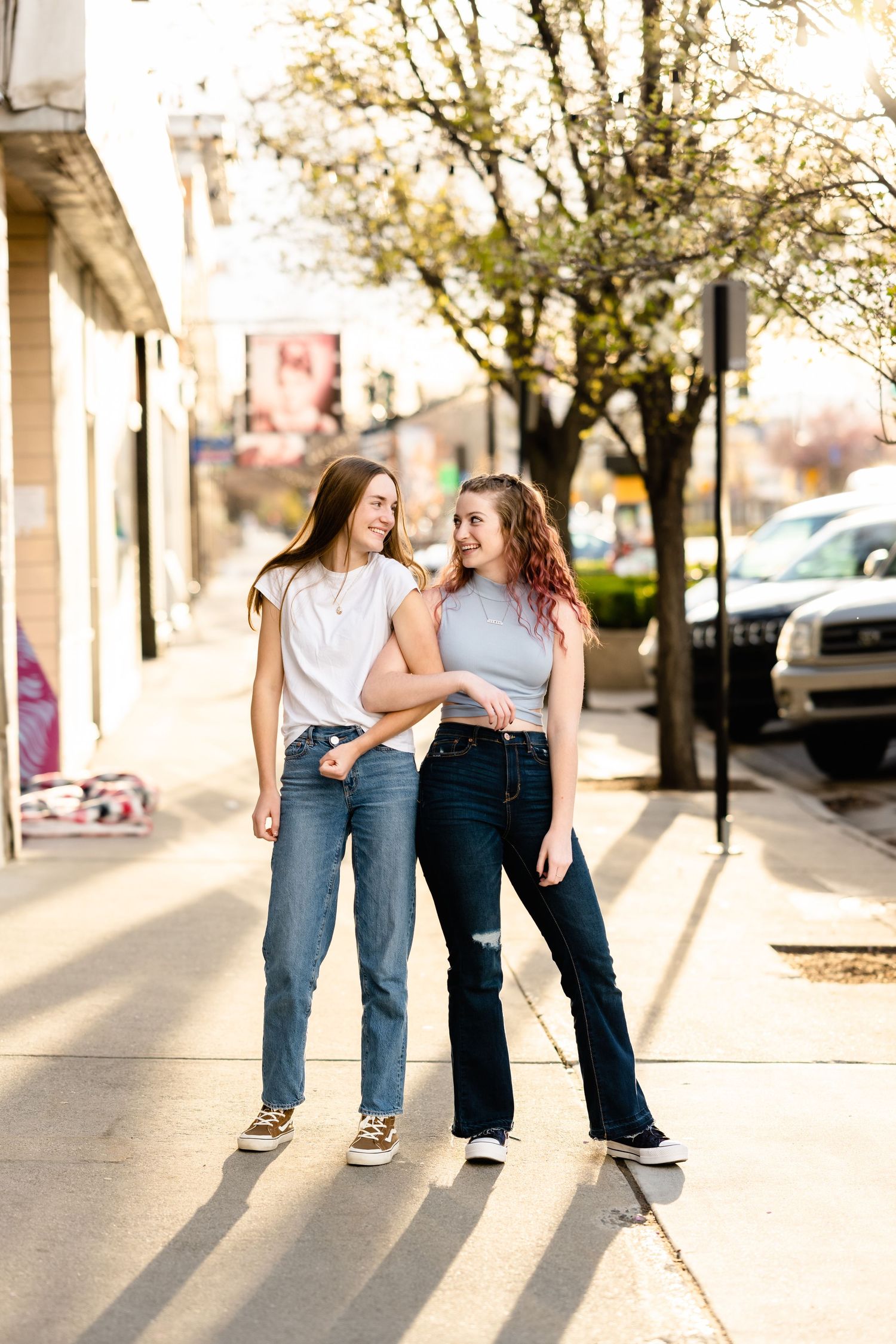 Two people in casual wear sit together on a curb in an urban setting during golden hour.