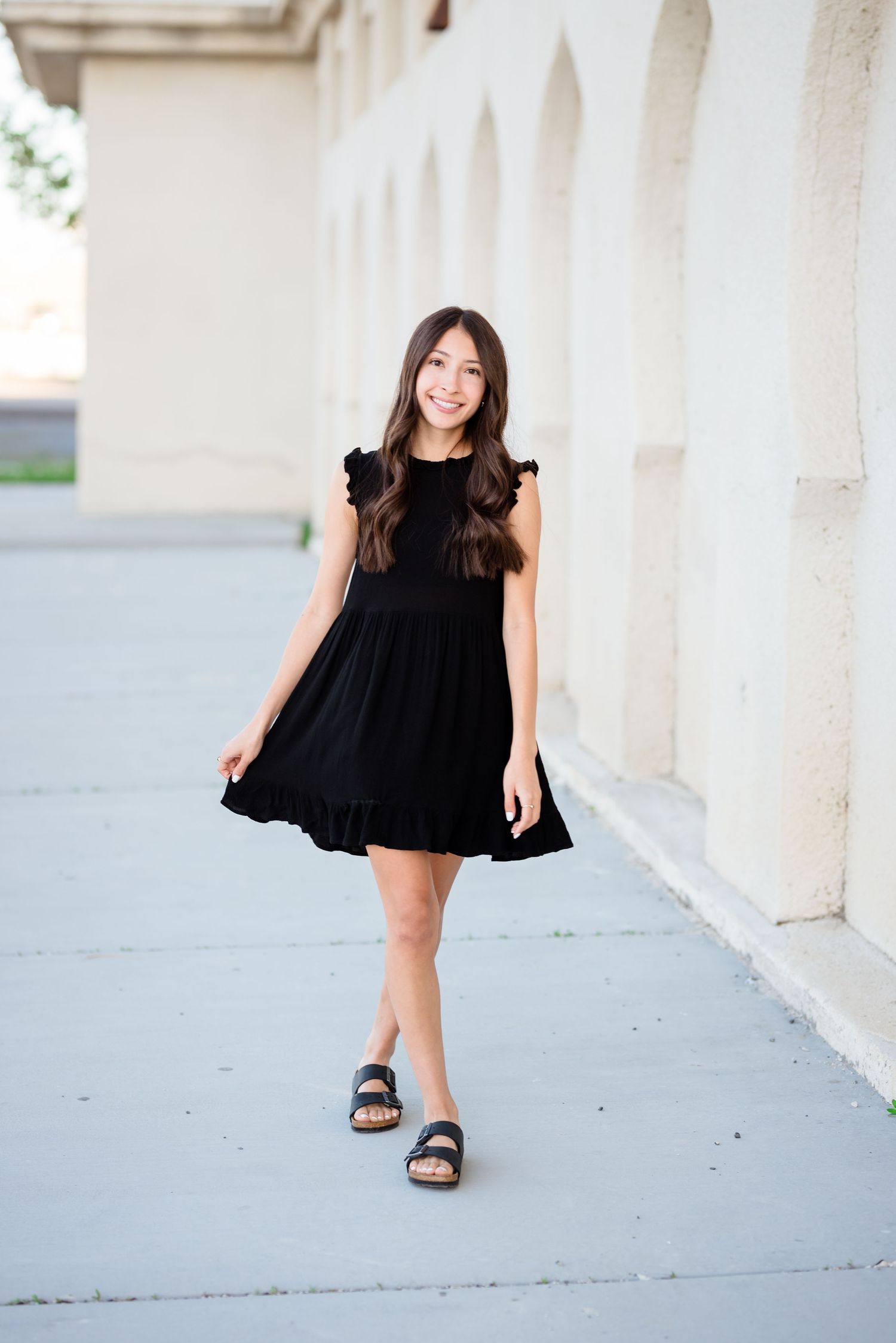 A sequence of photos showing a person in a flowing black dress posing playfully against a white architectural backdrop.