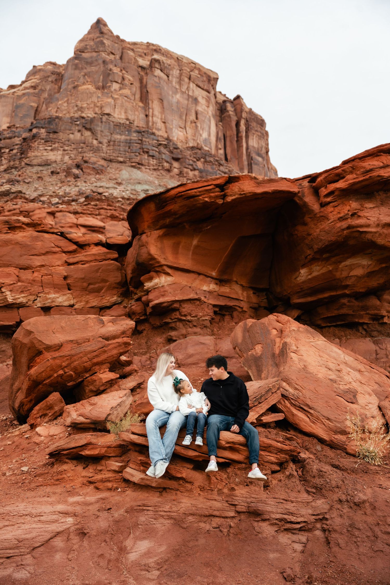 Family sitting together on red sandstone rock formations in a desert landscape.