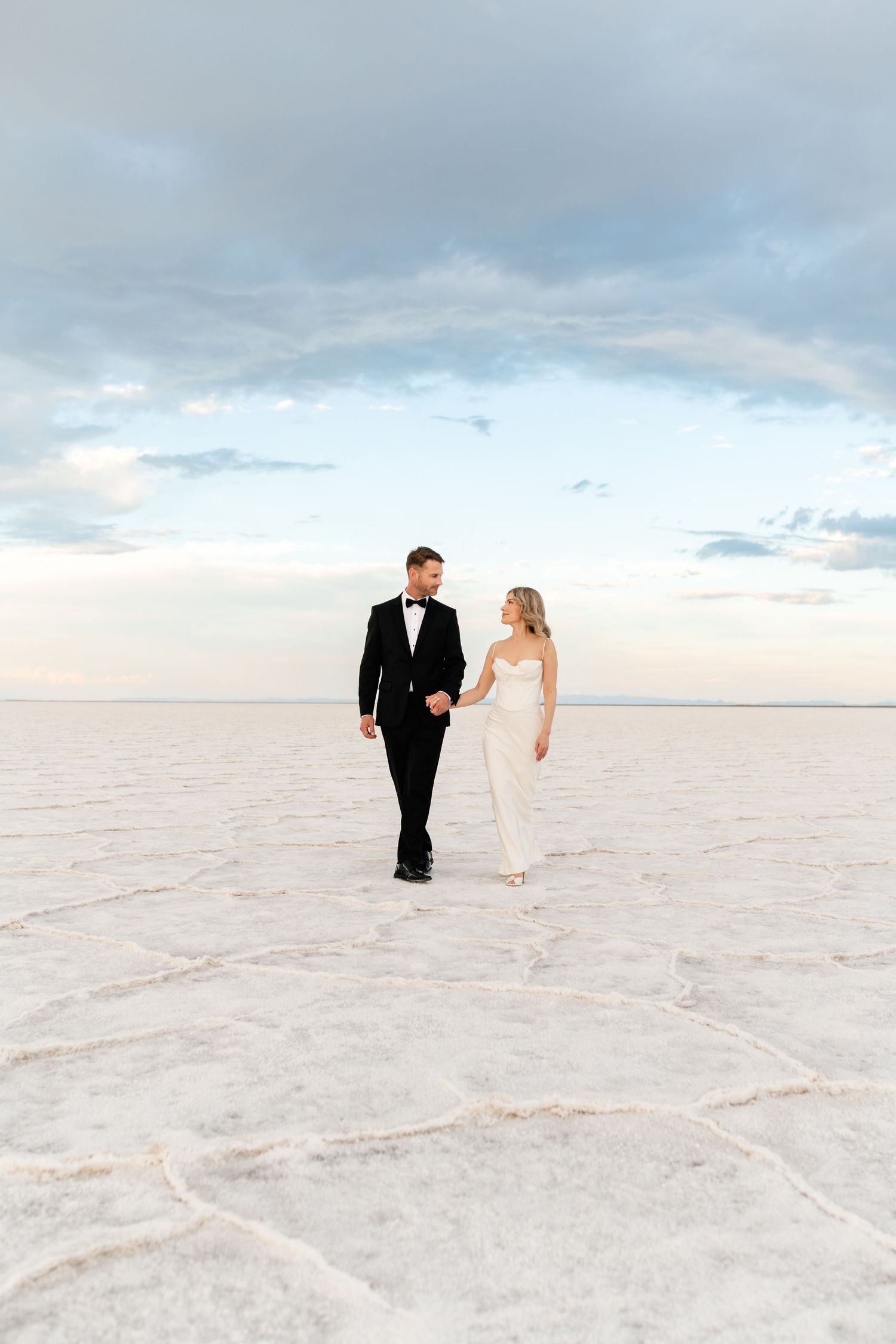 Salt Flats Elopement Photographer. A couple walks together across the pristine white salt flats under cloudy skies.