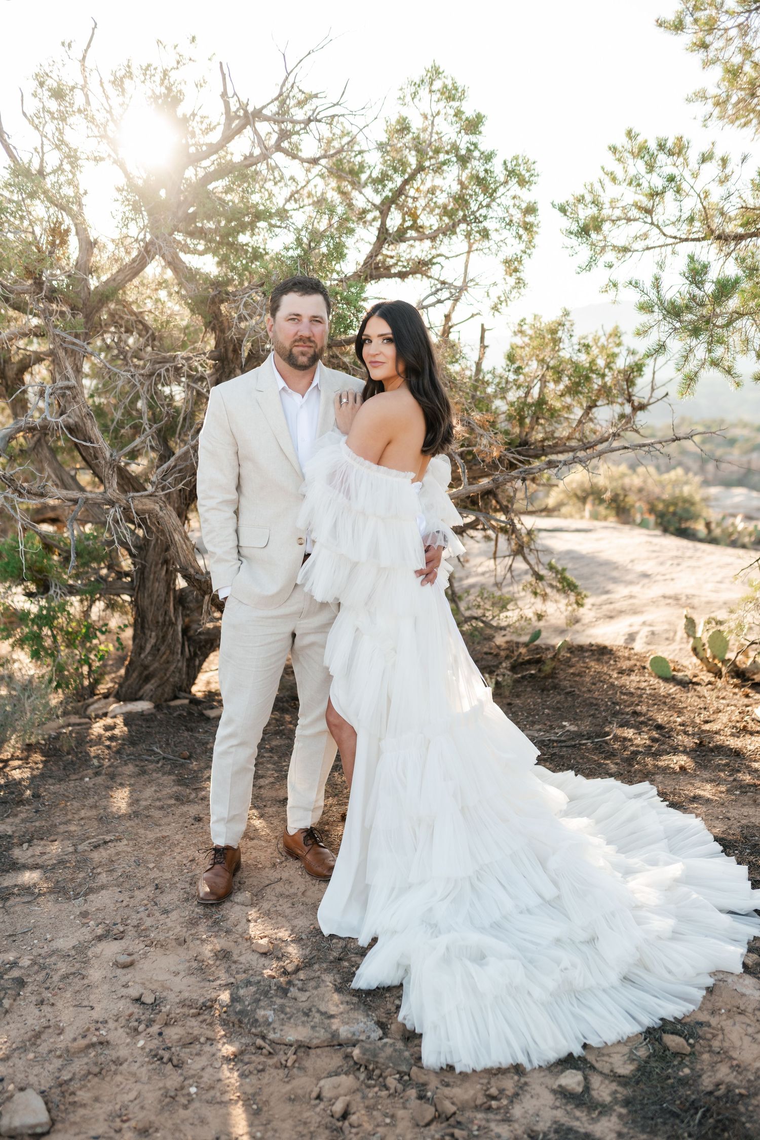 Zion destination photographer, Newlyweds in white share a romantic moment among desert trees during golden hour.