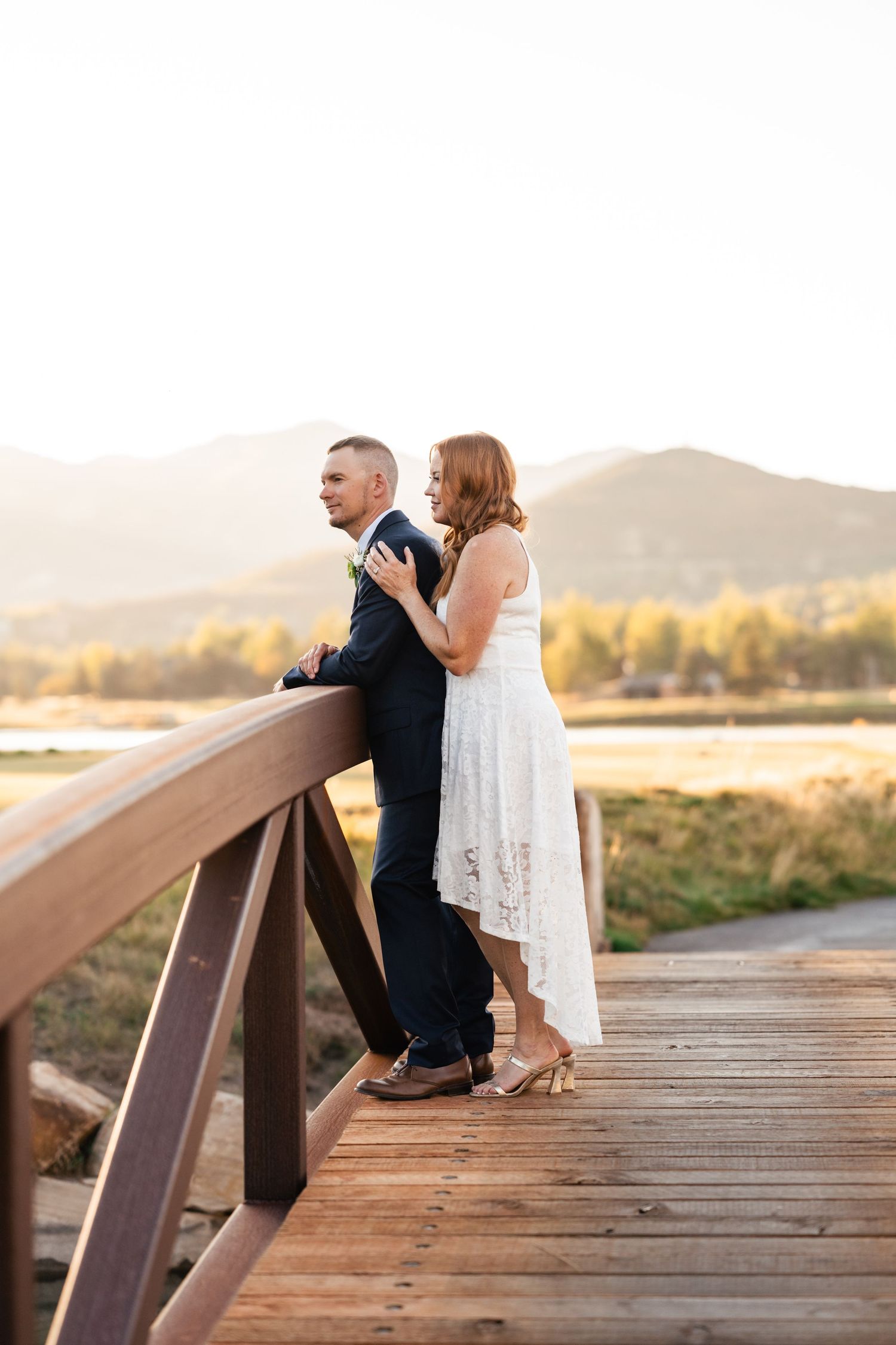 Romantic couple sits together on wooden bridge during golden sunset.