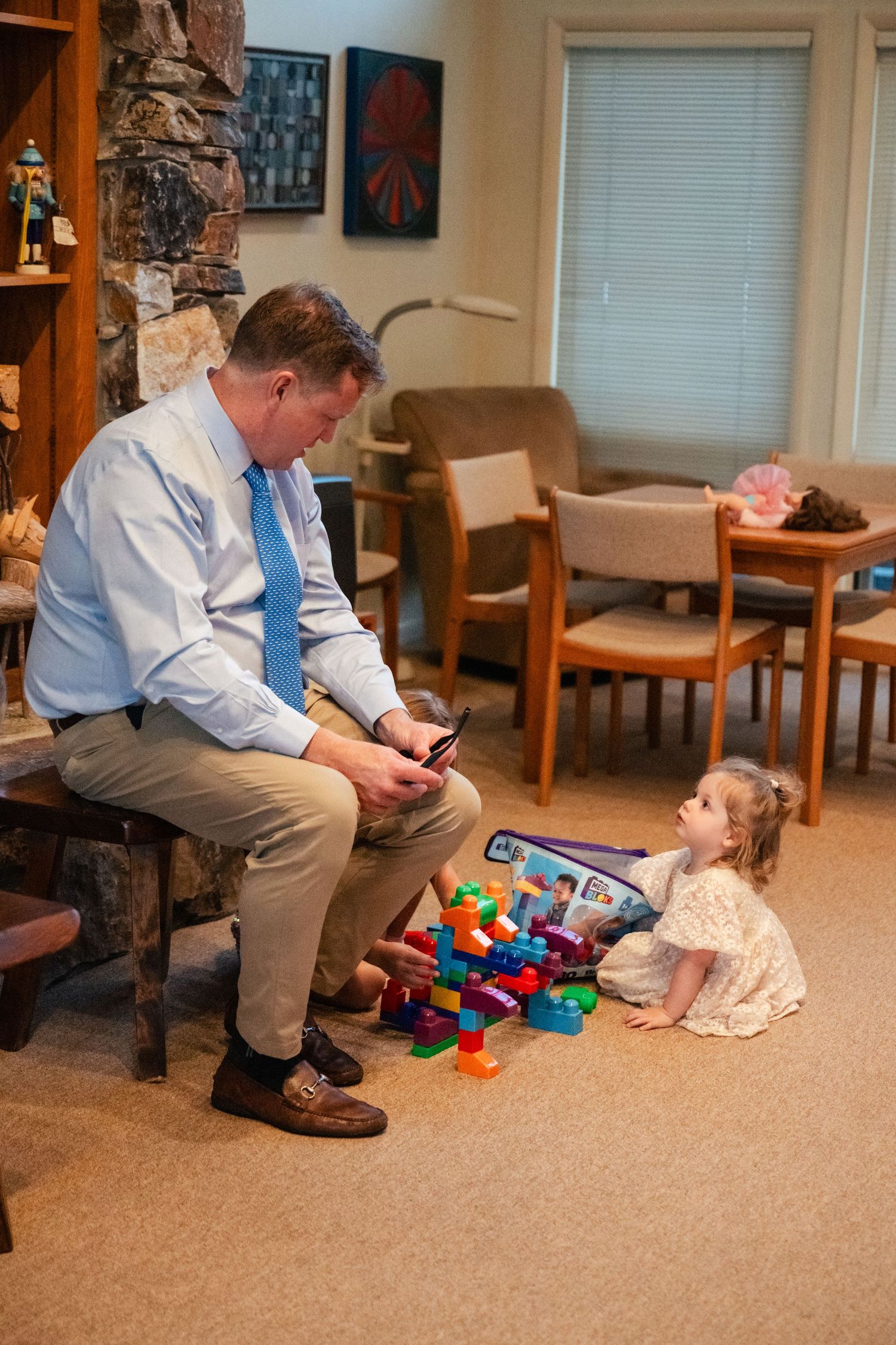 Man in blue shirt sits with child playing with colorful toys in living room.