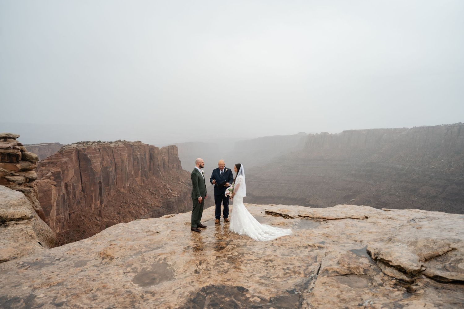 Panoramic view of a wedding ceremony taking place on a dramatic desert cliff edge.