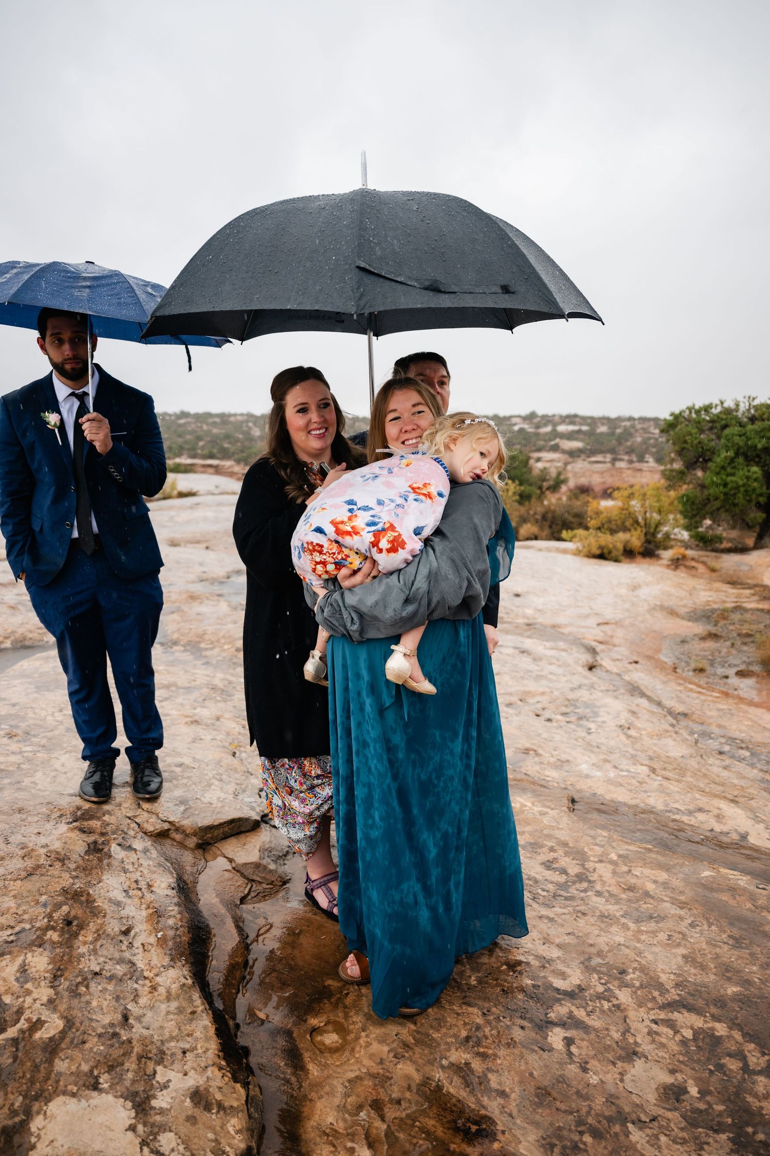 A group stands on rocky terrain under umbrellas during an overcast day.