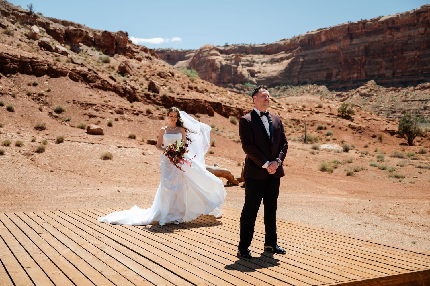 Bride and groom share a first look moment on a wooden deck surrounded by stunning red rock canyon scenery.