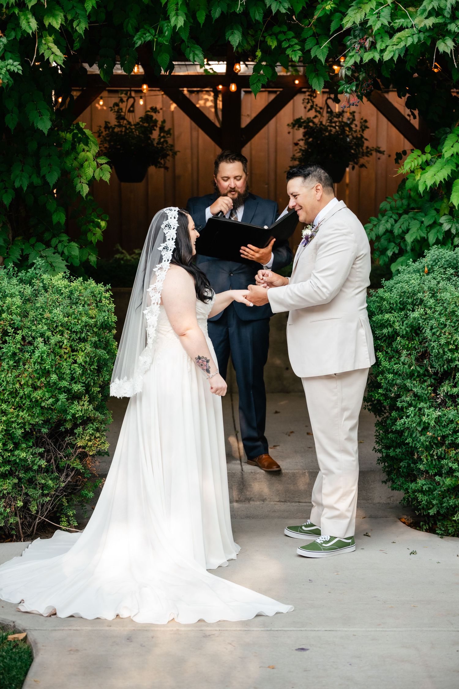 Wedding ceremony takes place under lush greenery with the couple exchanging rings as an officiant presides.
