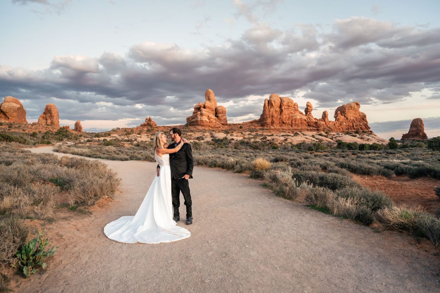 Wedding couple holds each other at the Windows in Arches NP on their elopement day by Utah Elopement Photographer