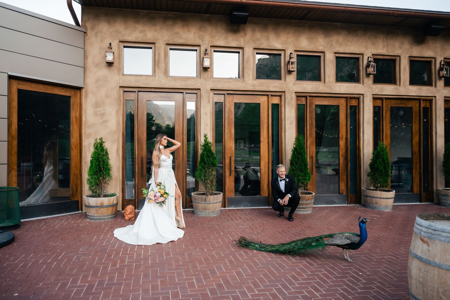Elegant venue exterior with glass doors, peacocks, and wine barrels creating an upscale rustic ambiance.