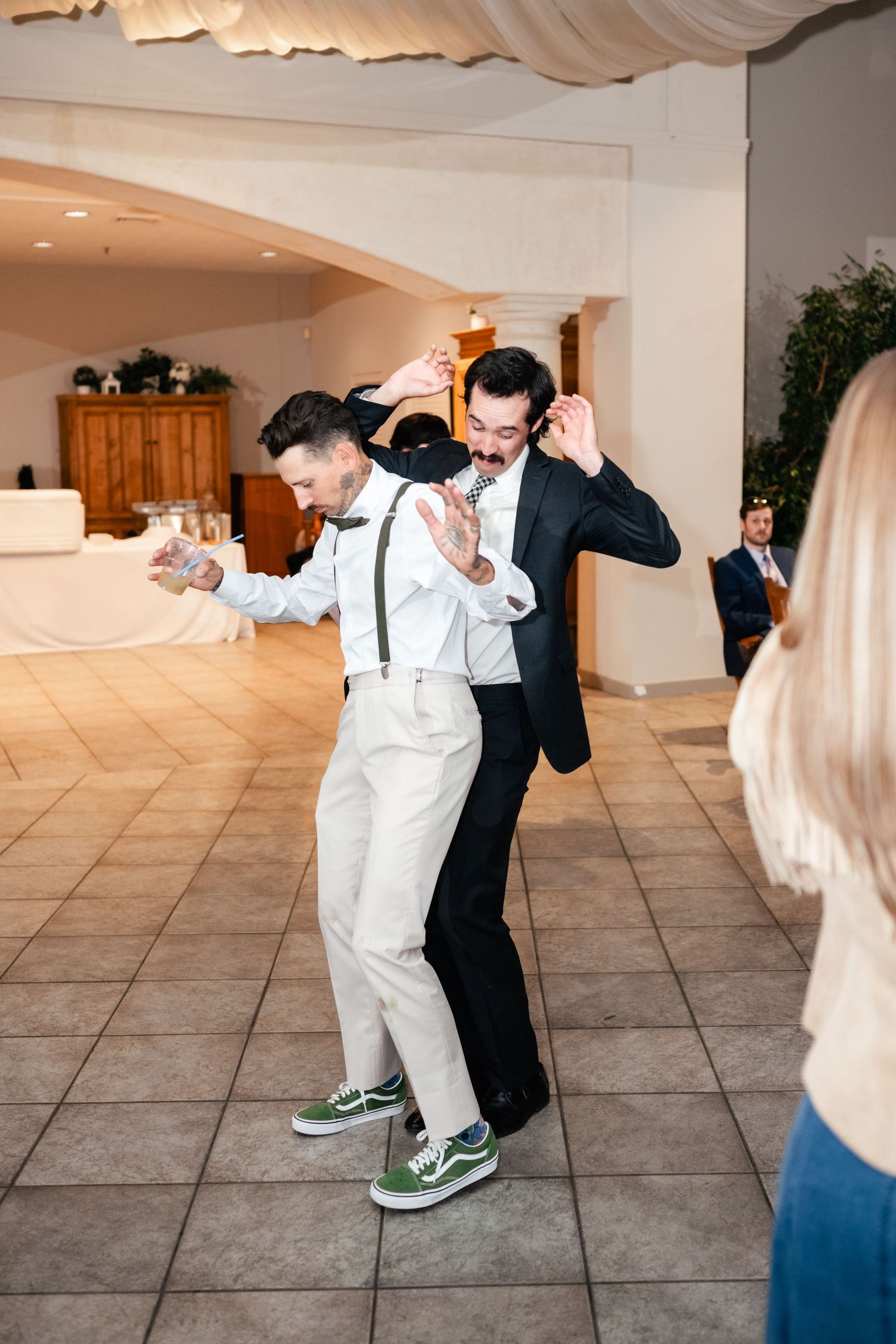 Two guests dancing energetically in formal attire with one wearing white and the other in a black suit.