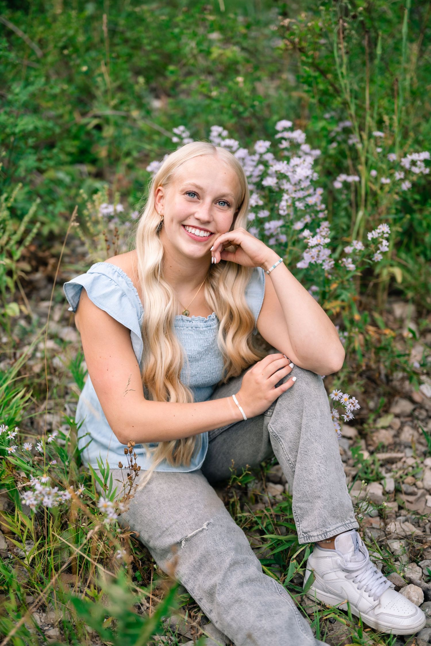 senior girl sitting near wildflowers and smiling for her senior pictures